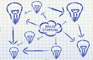 A hand-drawn diagram on graph paper showing a central cloud labeled “Brain Storming,” with arrows pointing to and from multiple light bulbs.